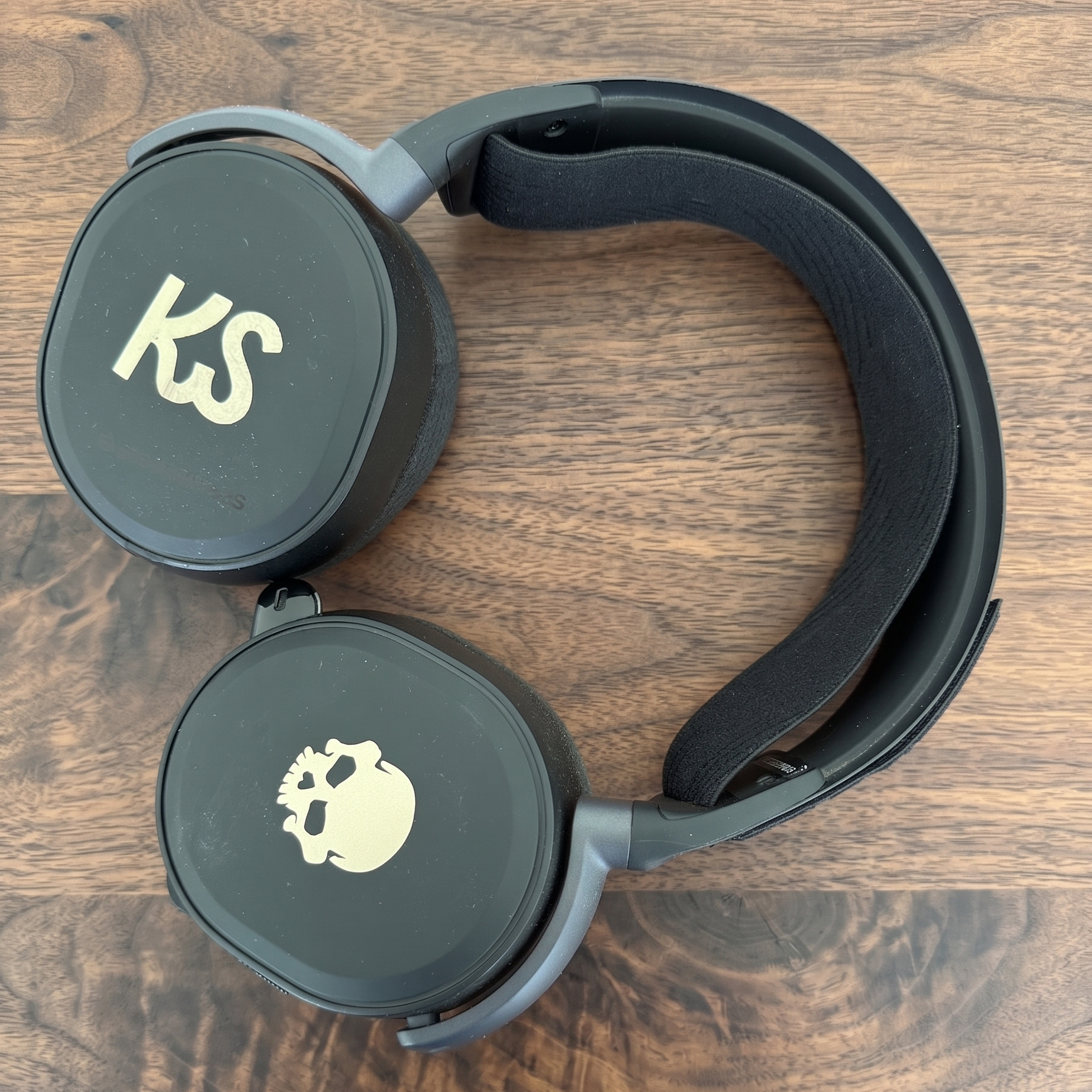 Black over-ear headphones with gray accents and skull-and-crossbones graphics on the earcups, photographed on a wooden surface.